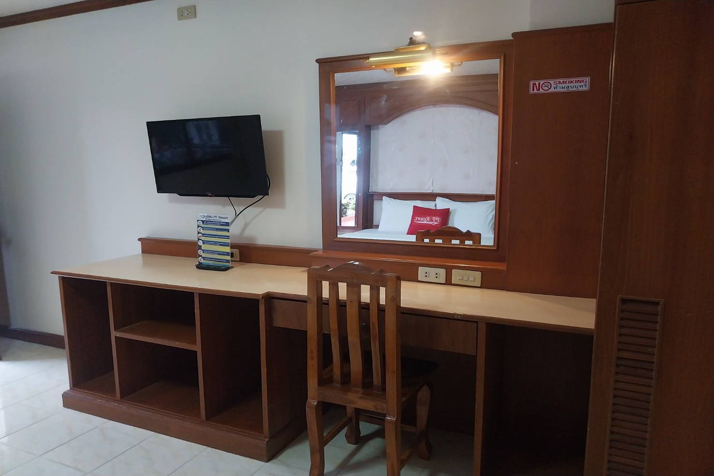 A room with a wooden desk, a chair, a television mounted on the wall, and a bed with a headboard.