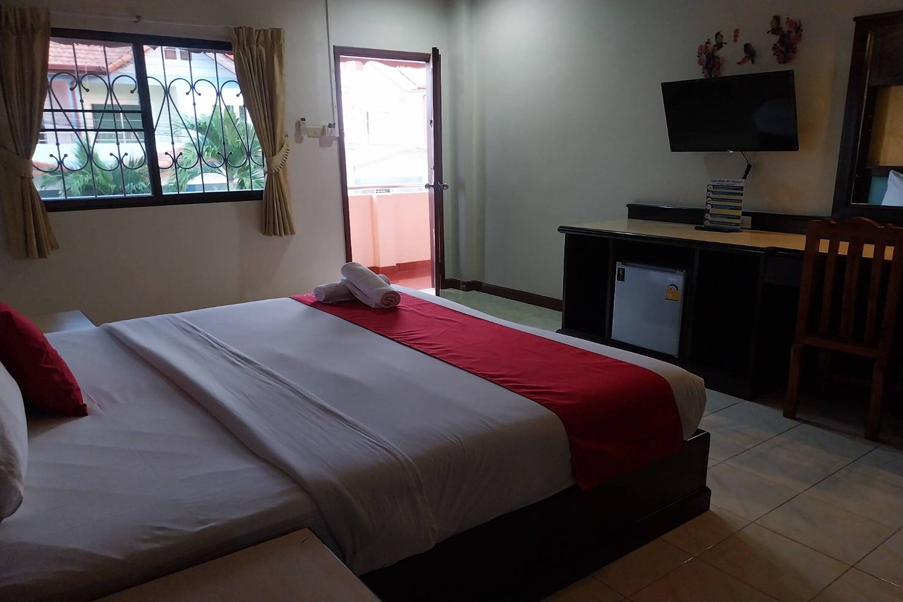 Habitación de hotel con cama, escritorio, silla, televisor y un refrigerador pequeño.
