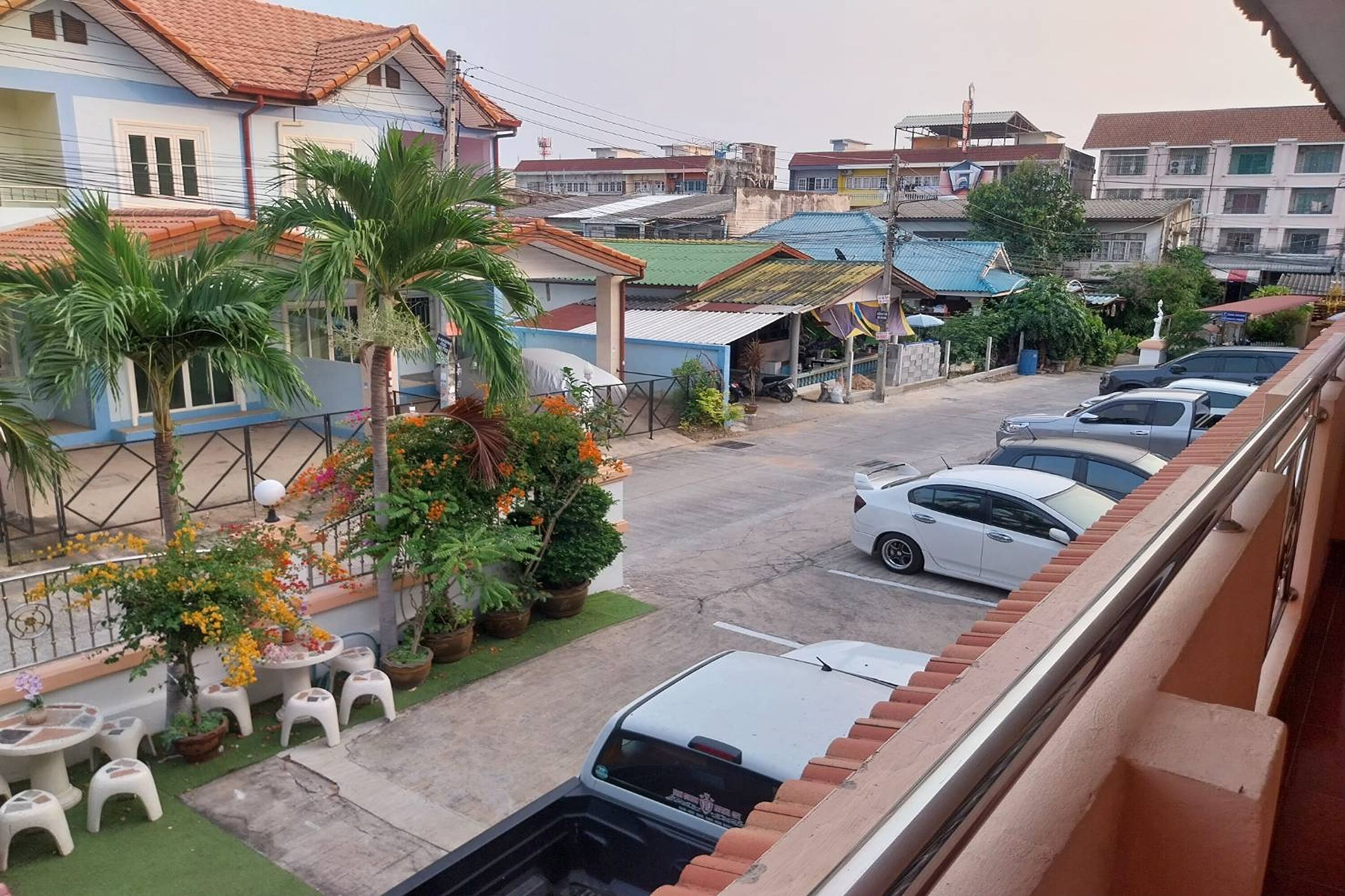 Eine Wohnstraße mit geparkten Autos, einer Reihe kleiner weißer Häuser und einem Balkon mit Blick auf die Straße.