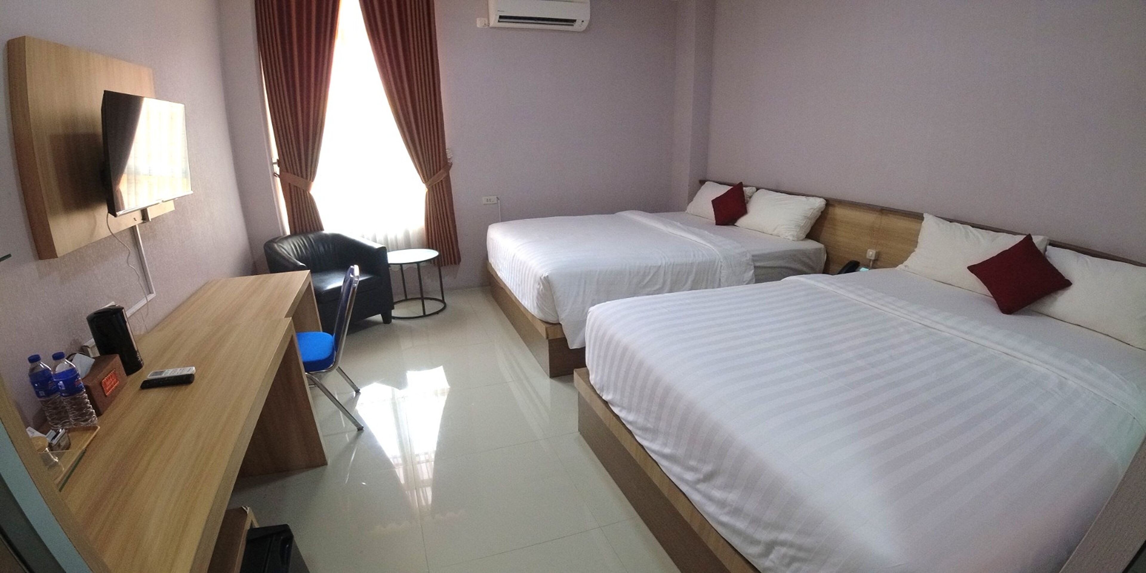 A hotel room with two beds, a desk with a chair, a TV, and a window with curtains.