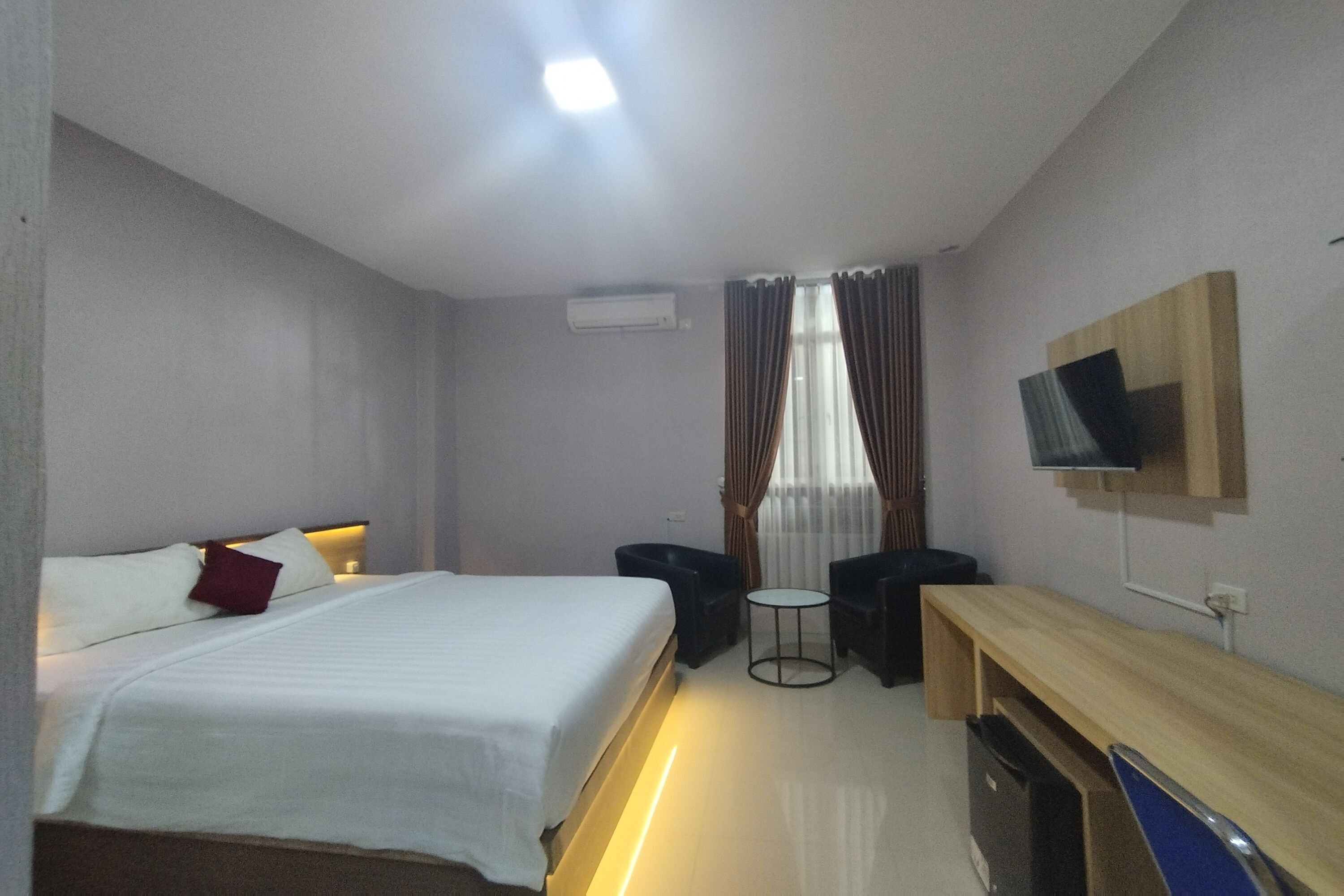 Habitación de hotel con cama, escritorio, silla, televisor y ventana con cortinas.
