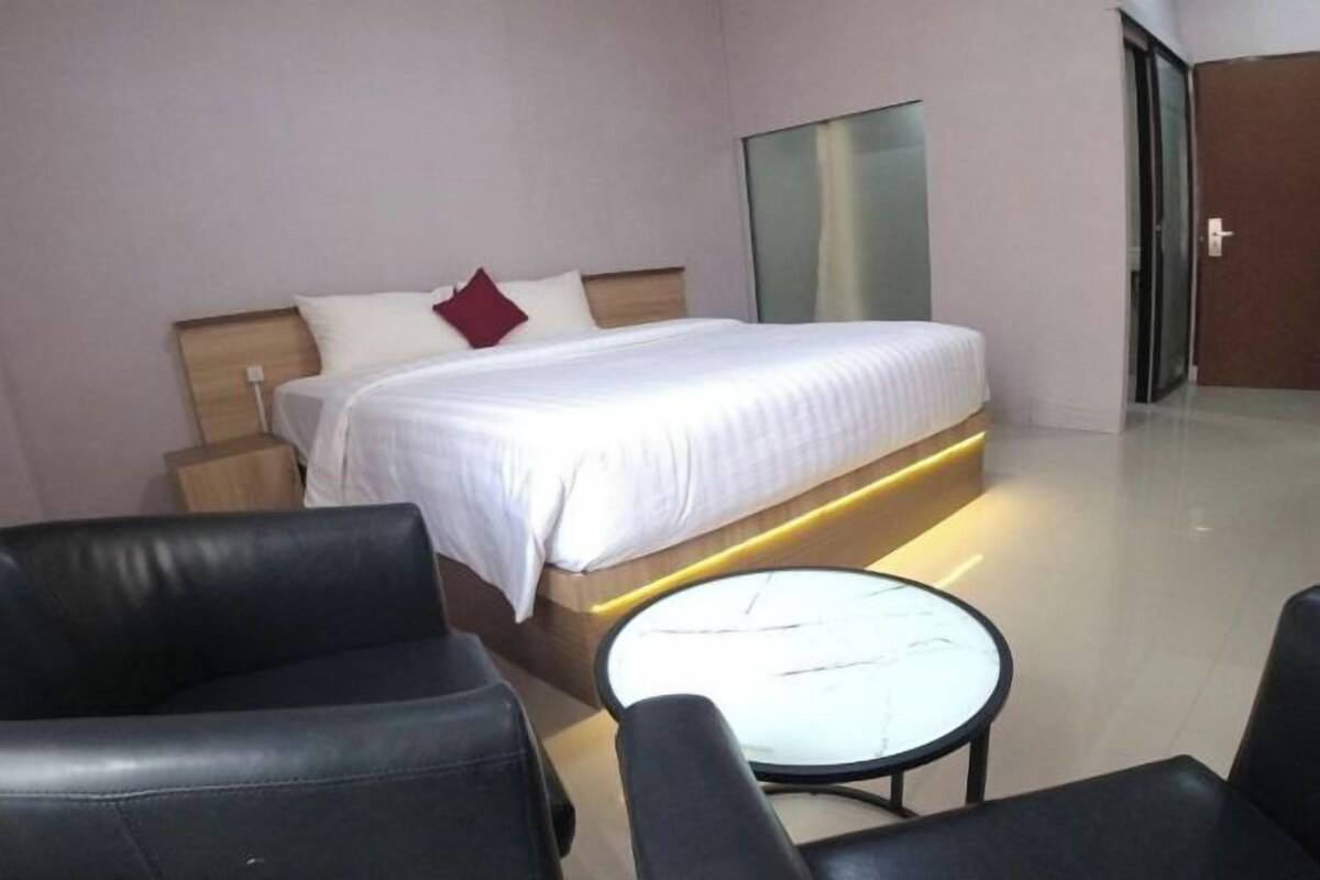 A hotel room with a bed, a bedside table, a round table, and two black leather chairs.