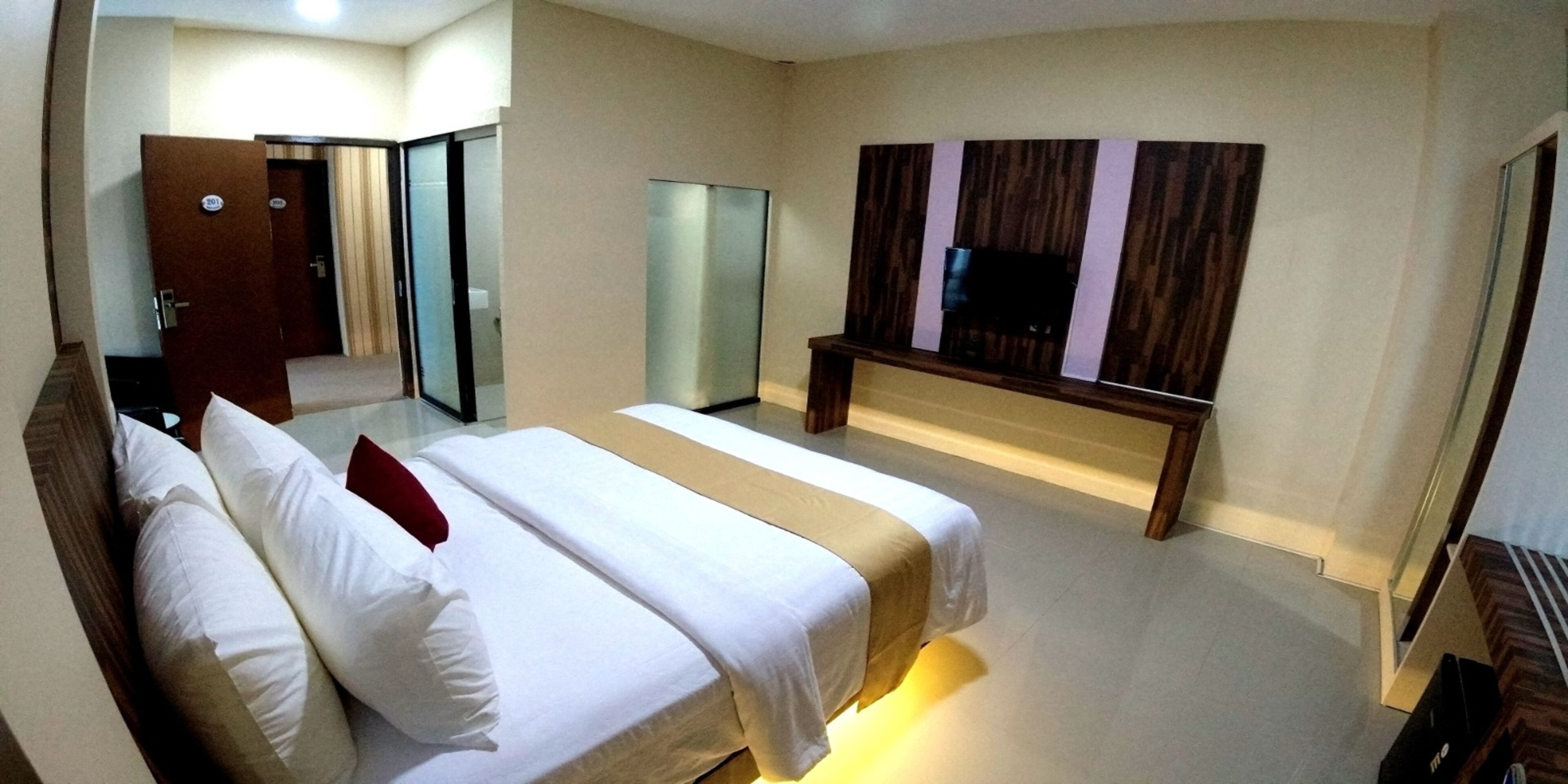 Une chambre d’hôtel avec un grand lit, un téléviseur fixé au mur et un miroir.