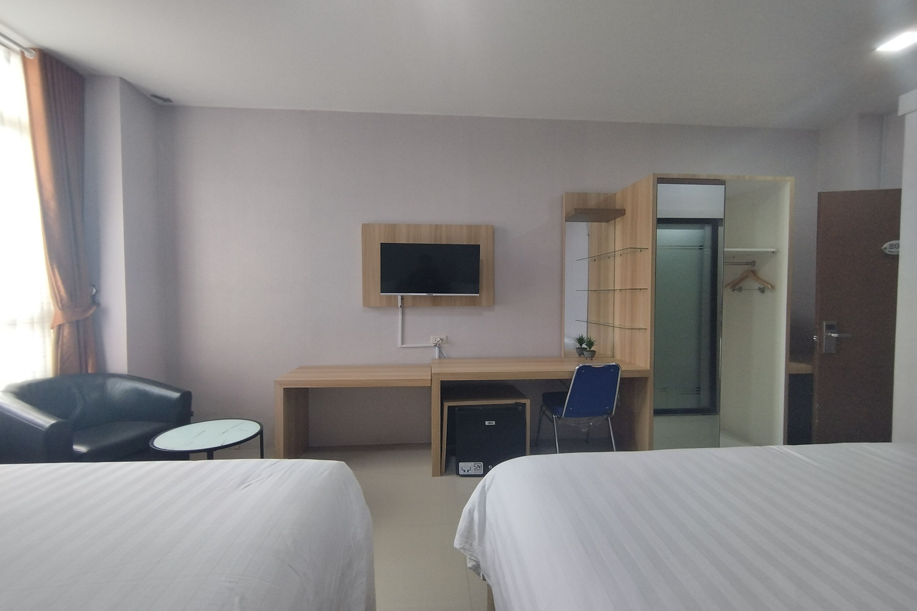 A hotel room with two beds, a desk, a chair, a TV, and a wardrobe.