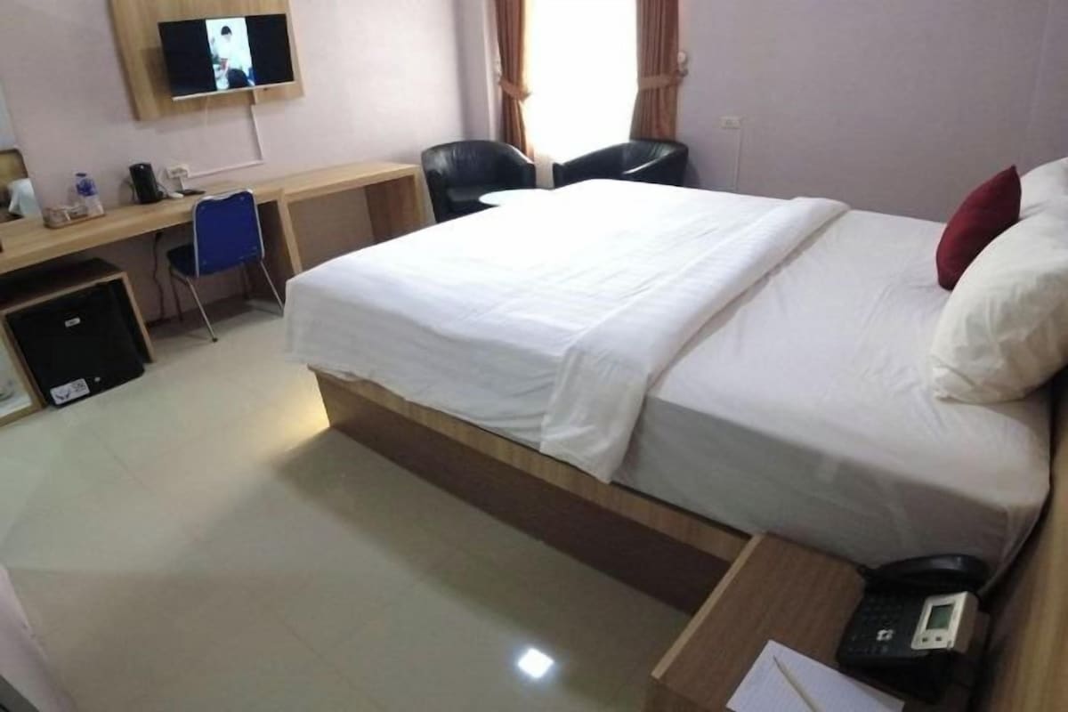 A hotel room with a bed, desk, chair, TV, and a phone.