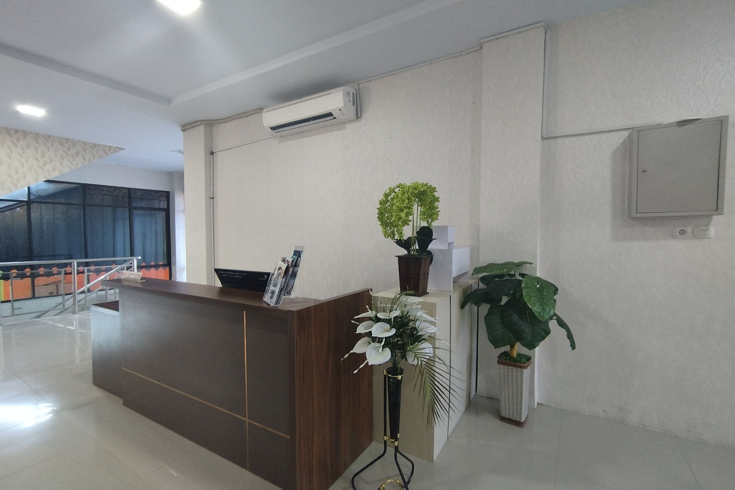 A reception area with a wooden reception desk, a potted plant, and a large potted plant to the right.