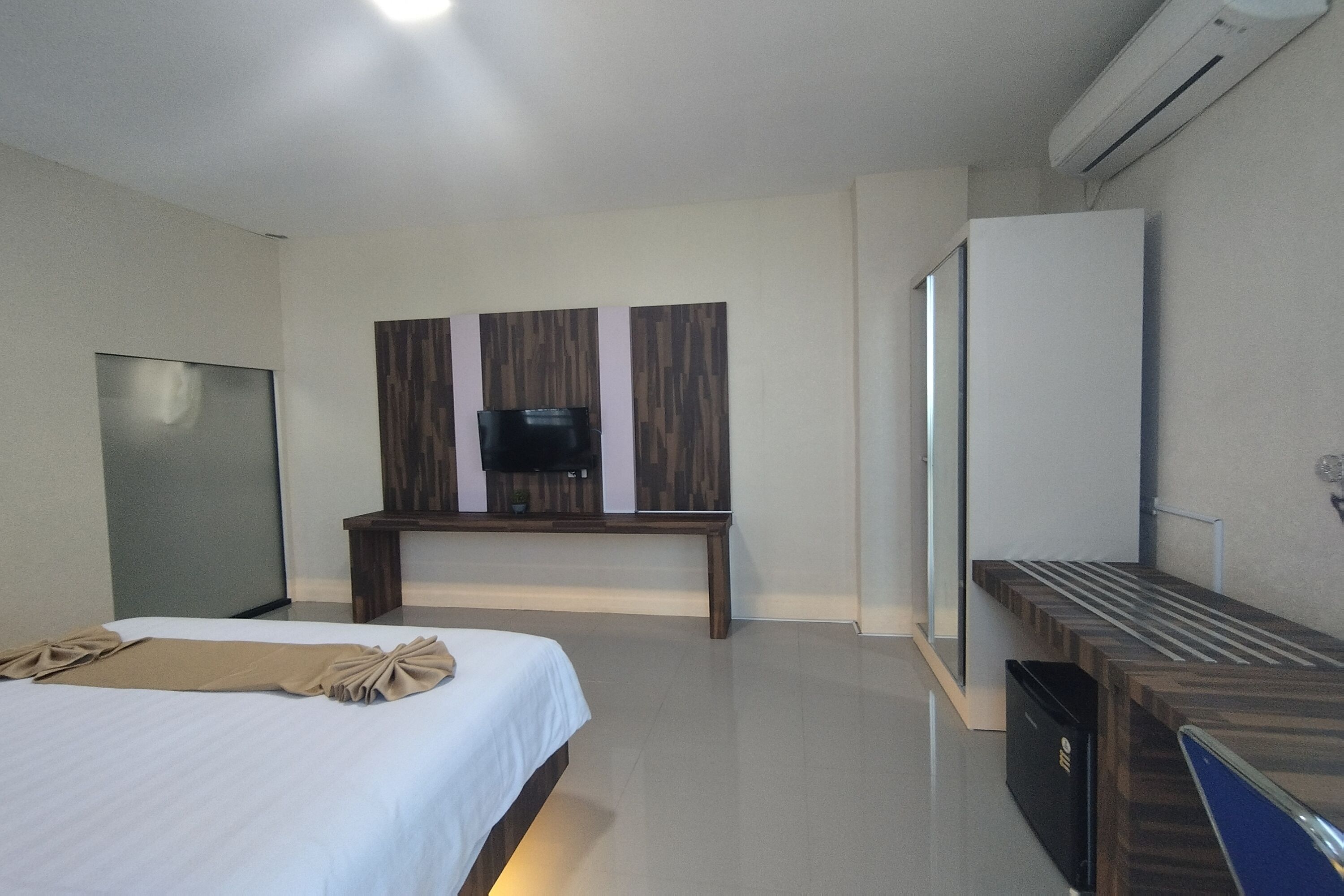 A modern hotel room with a bed, a TV on a wooden stand, a wardrobe, and a desk with a chair.