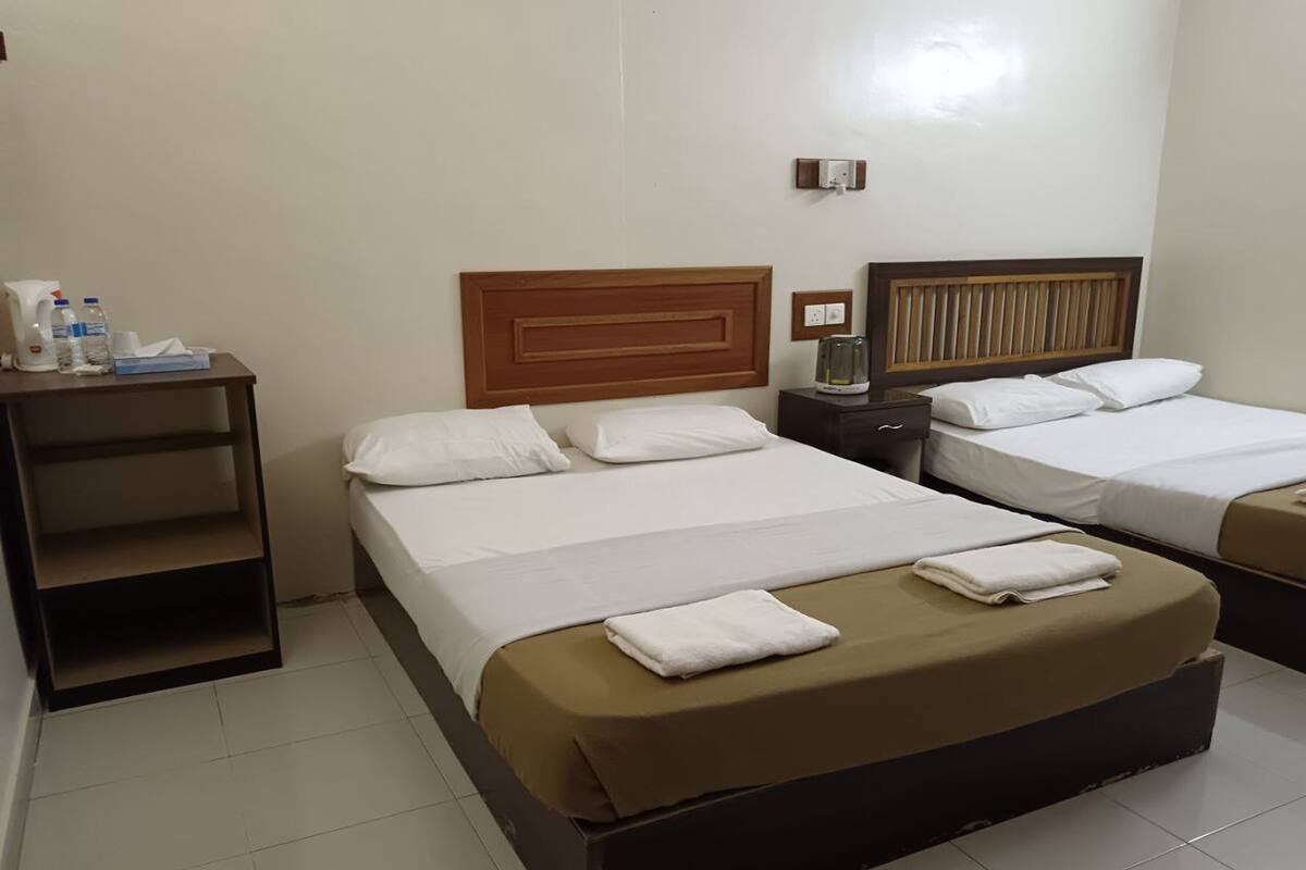Quarto de hotel com duas camas, uma escrivaninha com artigos de higiene e uma mesa de cabeceira com abajur.