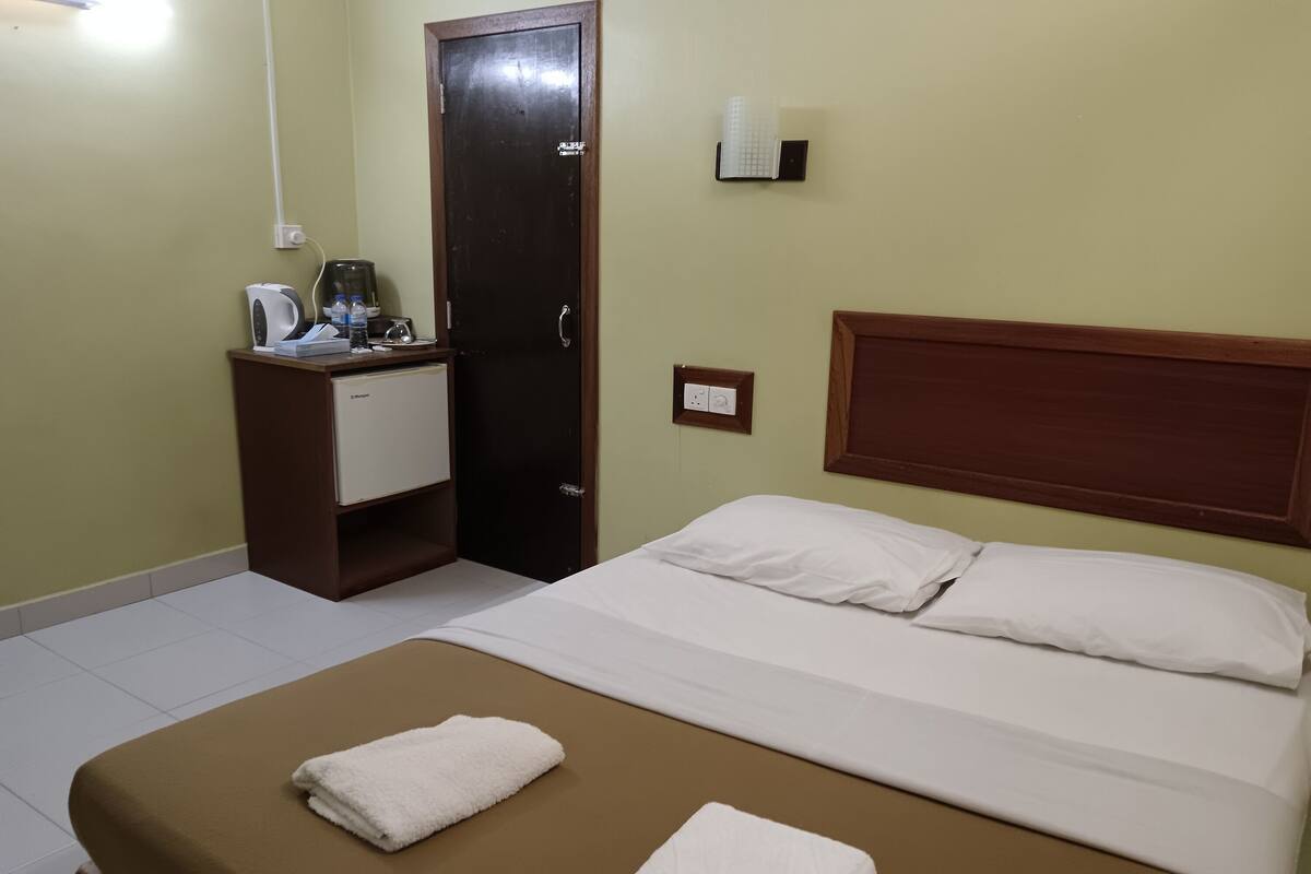 Quarto de hotel com cama, uma pequena mesa com cafeteira e uma porta.