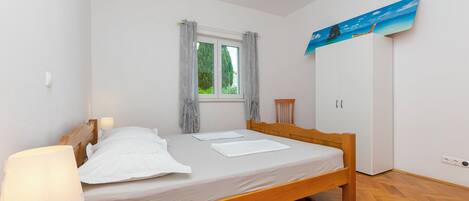 A neatly made bed with a wooden frame, a bedside lamp, and a window with curtains.