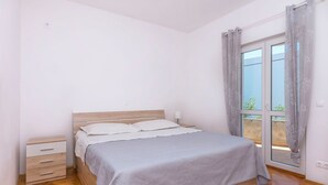 A bedroom with a bed, a nightstand, a drawer unit, and a window with curtains. - Apartment Duce Beach (Duce)