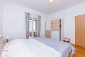 A bedroom with a bed, a window with curtains, a wardrobe, a bedside table, and a door. - Apartment Duce Beach (Dugi Rat)