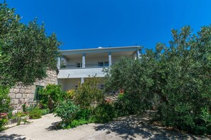 Un bĂątiment Ă deux Ă©tages dotĂ© dâun balcon, entourĂ© de verdure et surplombant un ciel bleu azur.