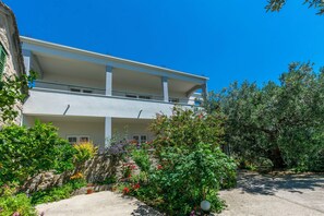 A two-story building with balconies, surrounded by lush greenery and flowering plants. - Apartment Duce Beach (Dugi Rat)