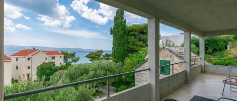 A balcony with a view of the sea and buildings, featuring a table and chairs.