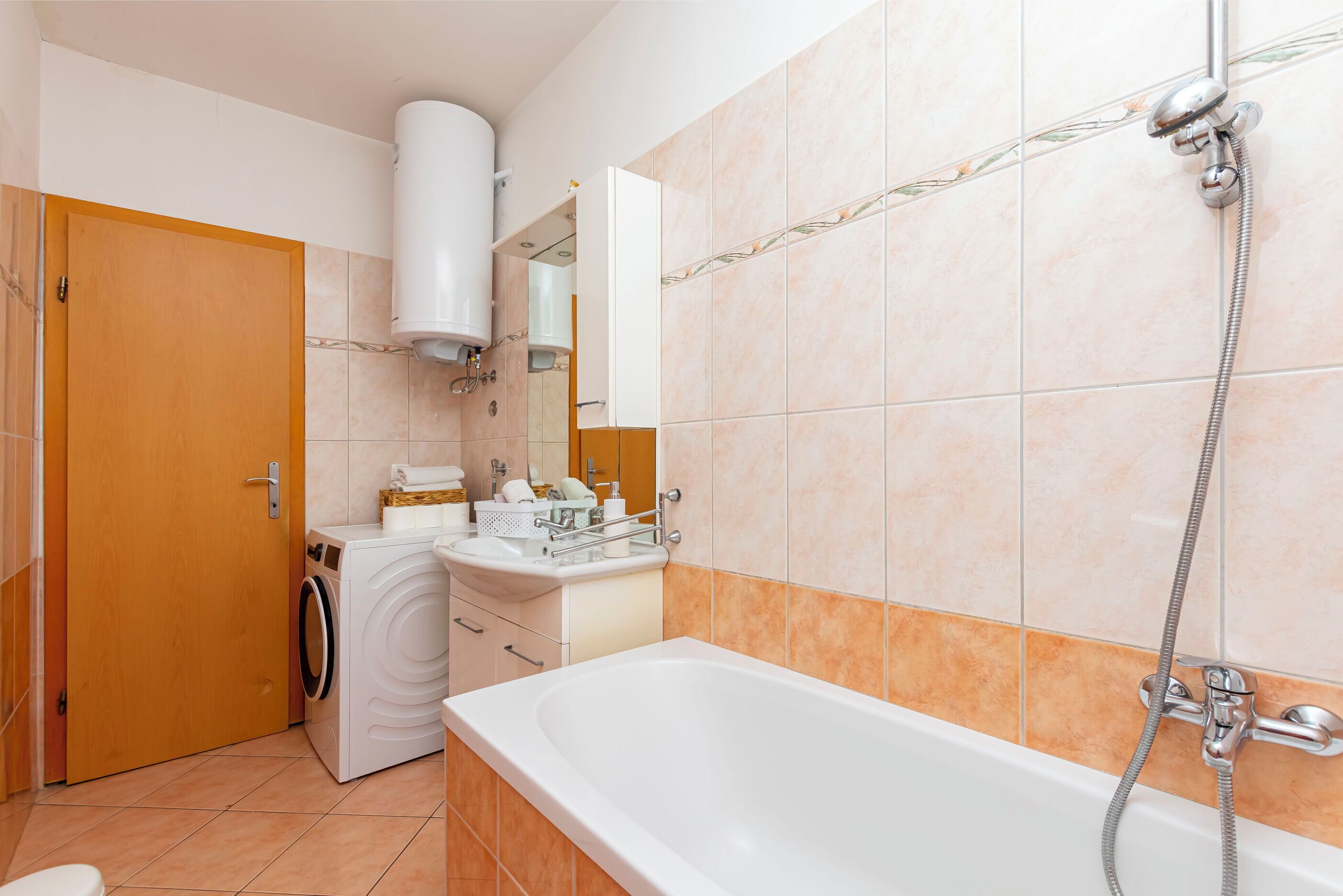 A bathroom with a washing machine, a sink, a mirror, and a bathtub with a showerhead.