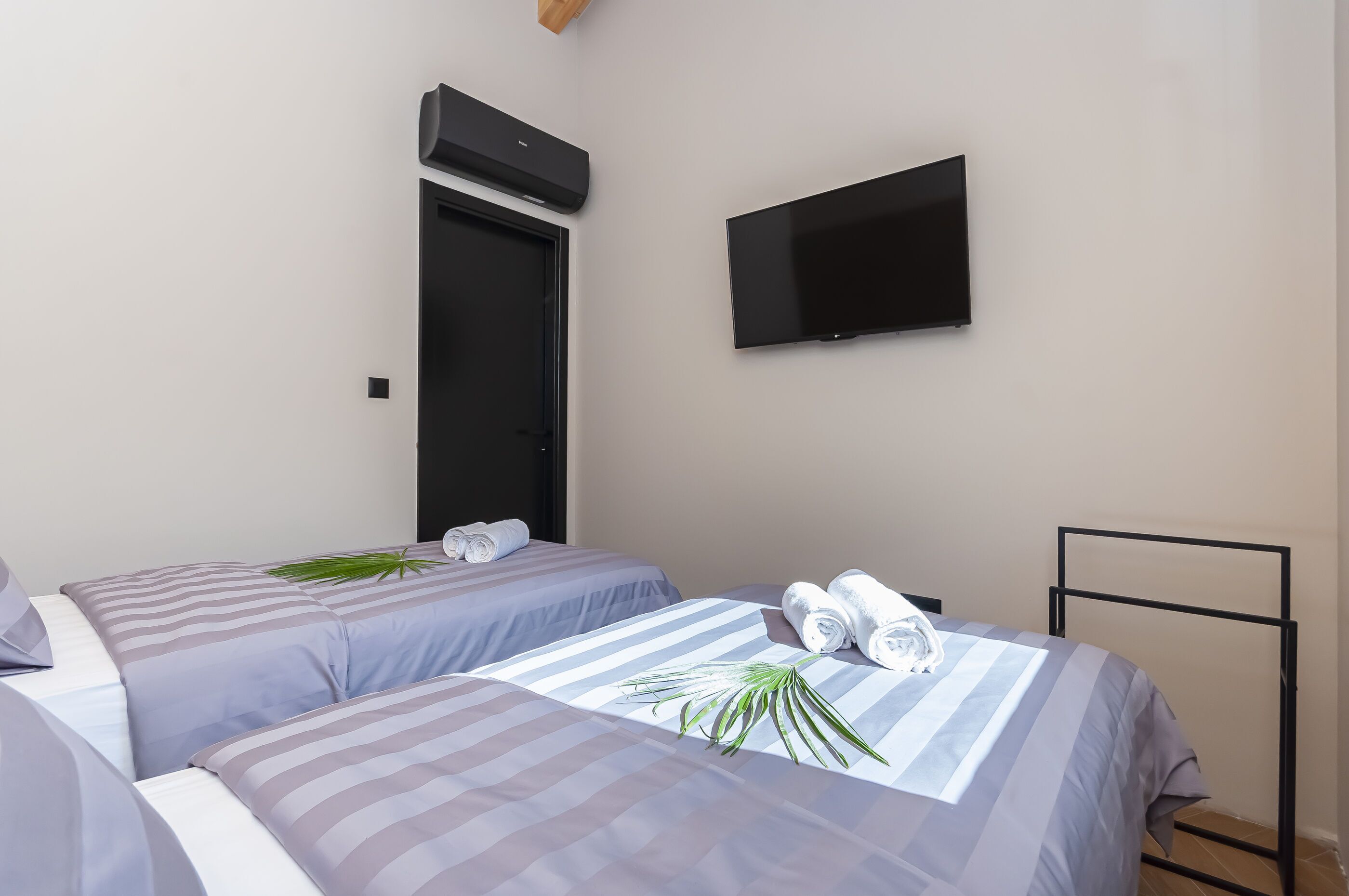 Une chambre d’hôtel avec deux lits, un téléviseur à écran plat fixé au mur et une porte surmontée d’un appareil de climatisation.