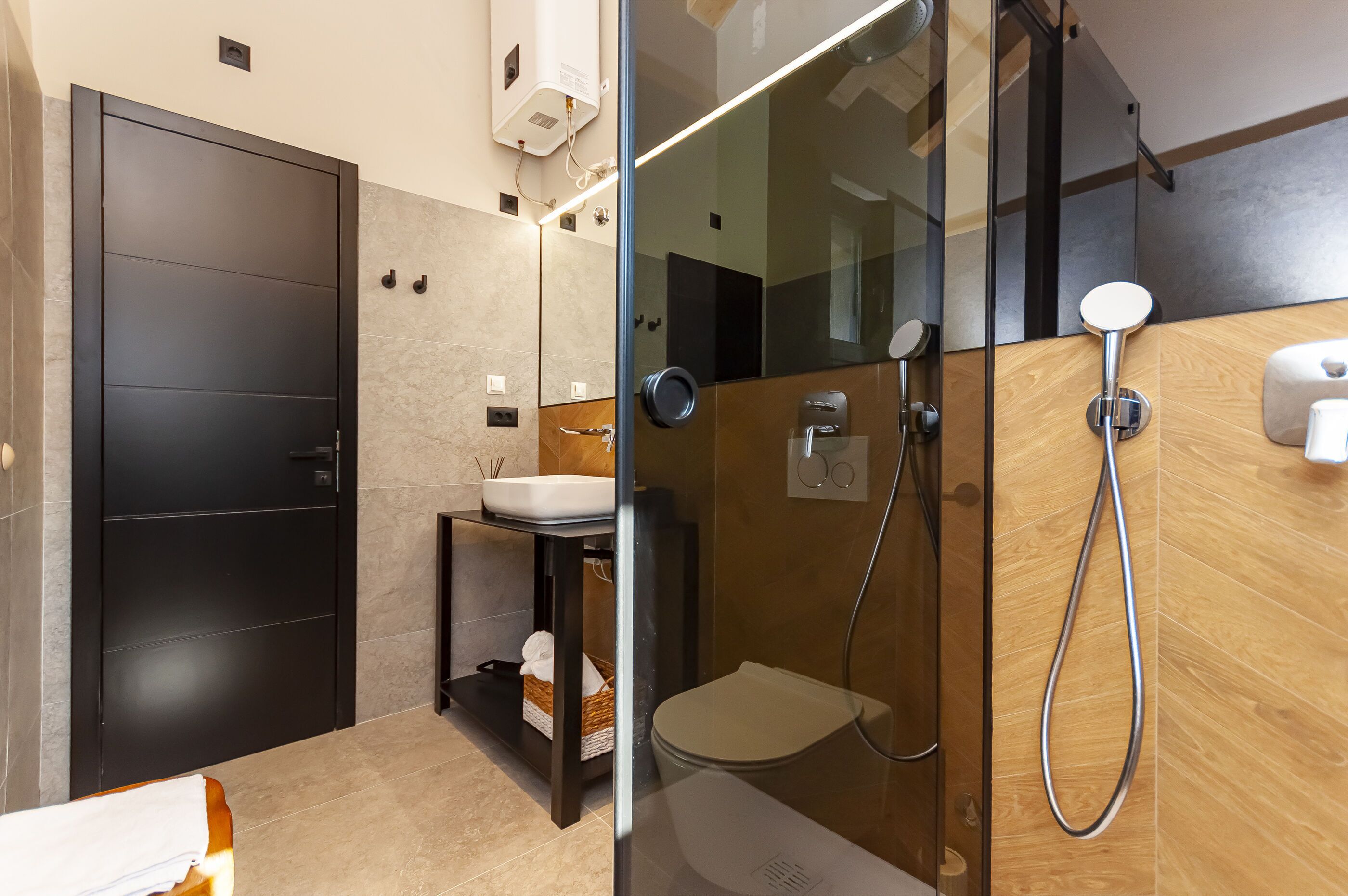 A modern bathroom with a glass-enclosed shower, a black door, a sink, and a wooden vanity.