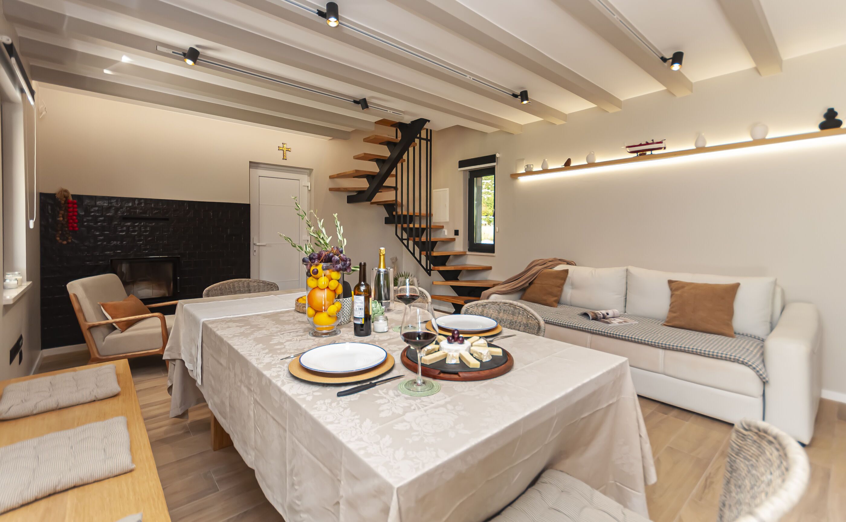 A modern dining area with a table set for two, a fireplace, and a staircase leading to an upper level.