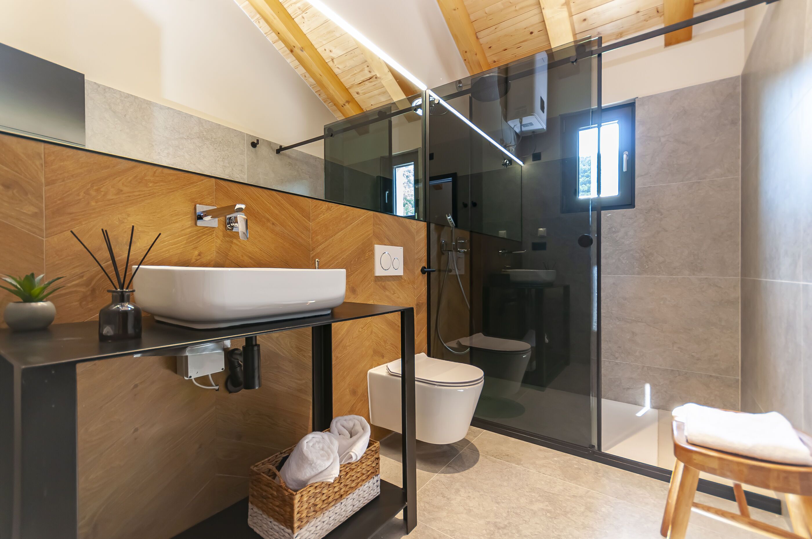 A modern bathroom with a glass shower enclosure, a white sink, and a wooden vanity.