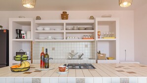 Een keuken met witte kastjes, een betegelde spatwand, een gasfornuis en een fruitschaal op het aanrecht.
