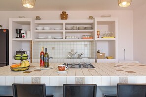 Una cocina con armarios blancos, salpicadero de azulejos, estufa a gas y un bol con fruta en la encimera.