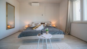 Een slaapkamer met een bed, nachtlampjes, een spiegel, een kleintje tafeltje met een plantje, en een raam met gordijnen.