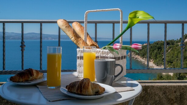 Ontbijt op een balkon met croissants, jus d'orange, een mok en een mand met brood.