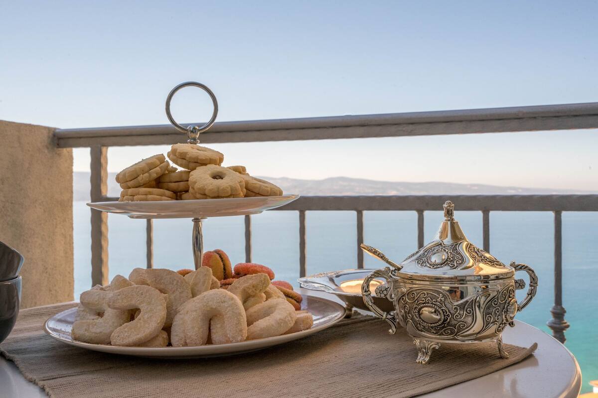 A tray of cookies and a decorative silver teapot on a balcony with a scenic view.