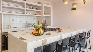 Een keuken met witte planken, een betegelde spatwand, een fruitschaal en barstoelen.