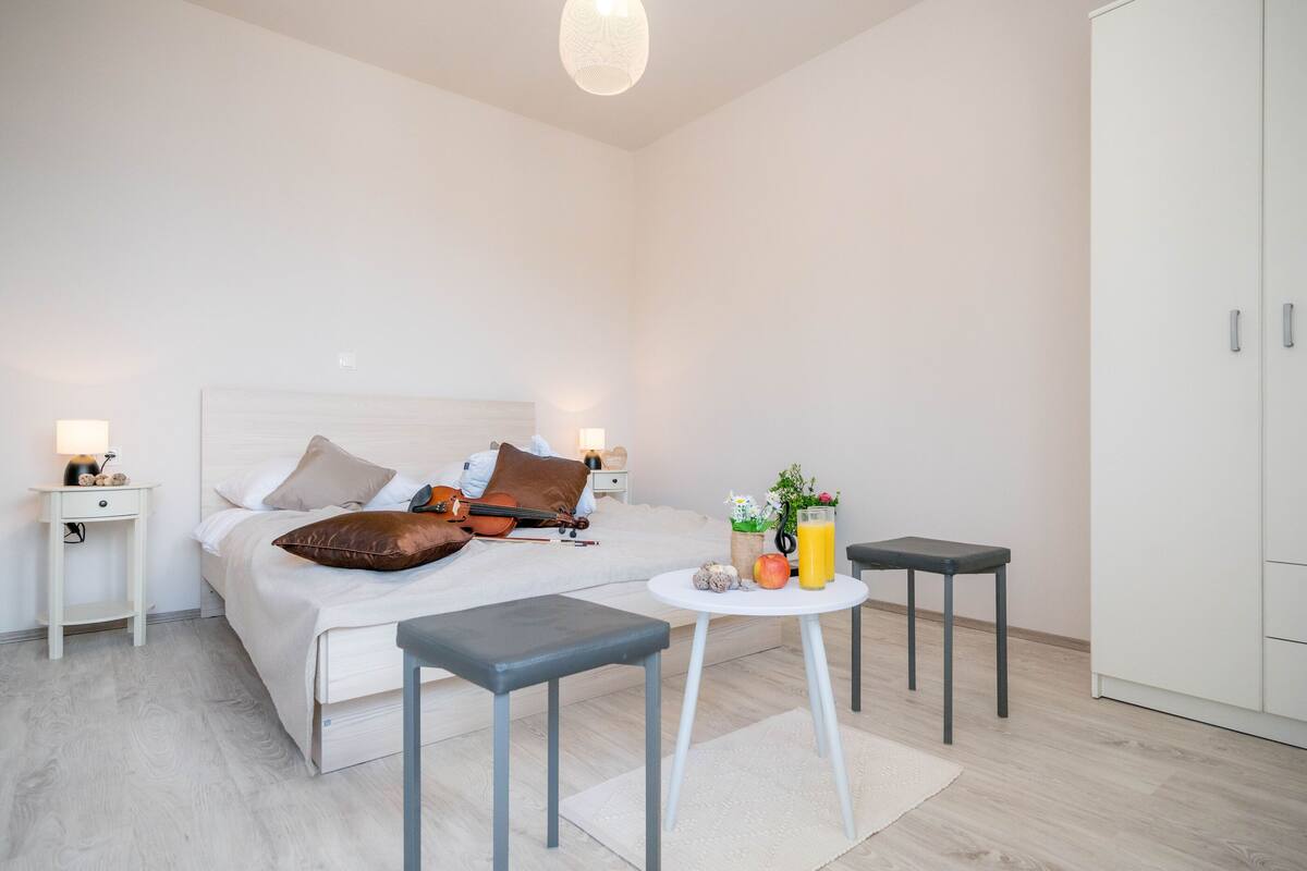 A modern bedroom with a bed, bedside tables, a small round table with a drink and fruit, and a wardrobe.