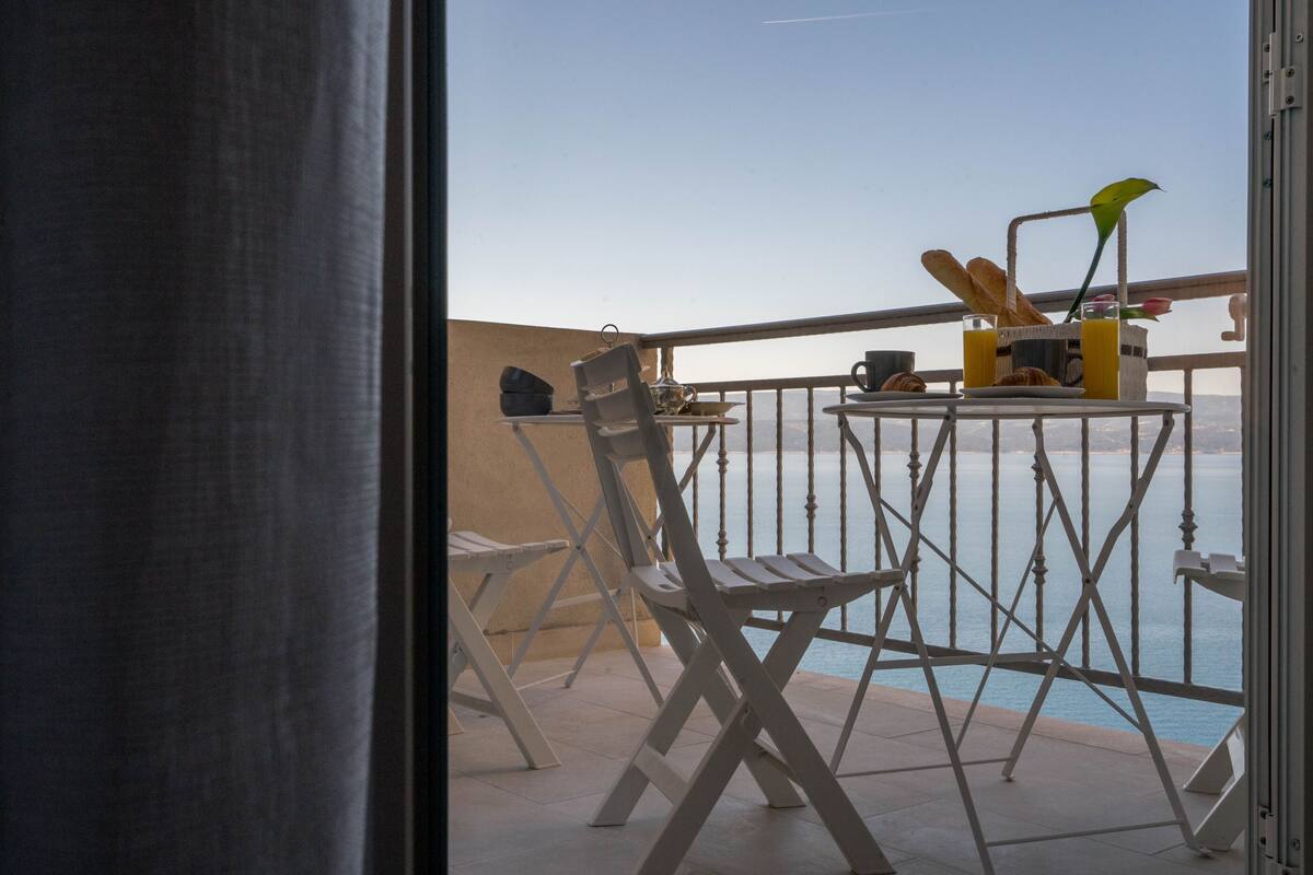 A balcony with a table set for breakfast, including bread, pastries, and a drink.