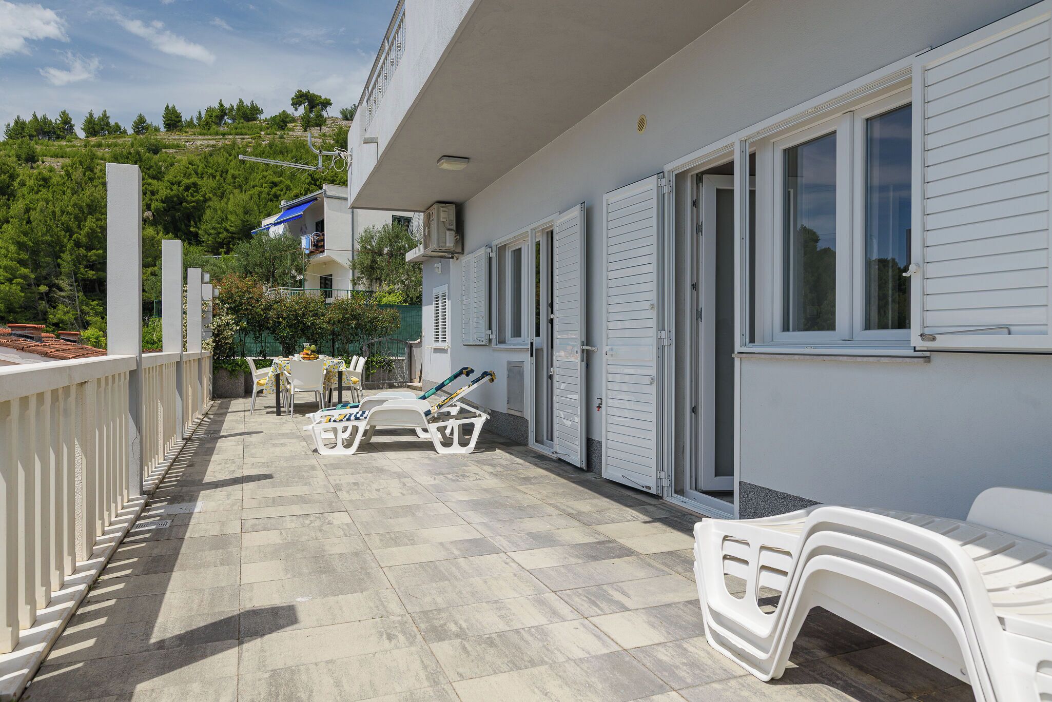 A balcony with white furniture, a tiled floor, and a view of a green hillside.
