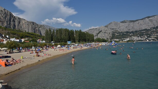 A beach with clear water, people sunbathing, and a mountainous backdrop. - Apartments Tonko (Duce)