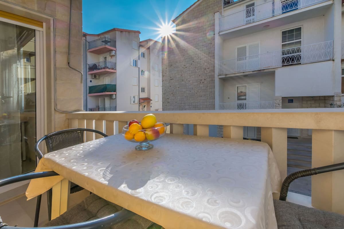 A balcony with a table and a fruit bowl, overlooking a residential building.