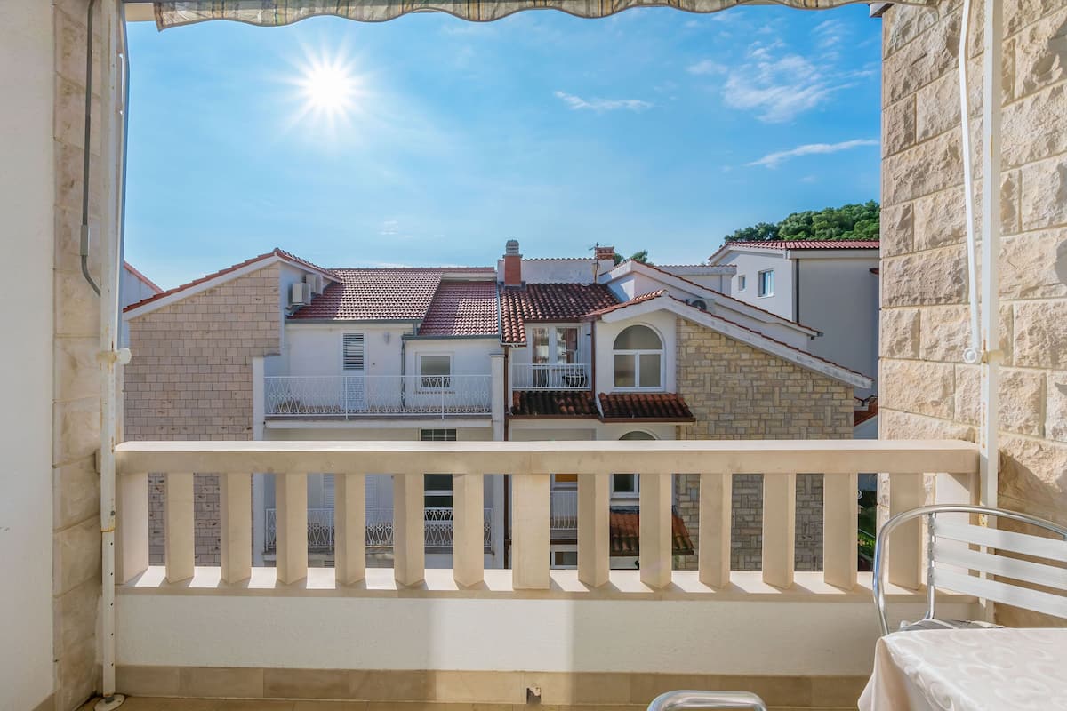 A balcony with a white railing overlooking a row of buildings with red-tiled roofs.