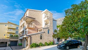 A two-story building with a balcony, a car parked in front, and a tree to the right. - Apartments Tonko (Duce)