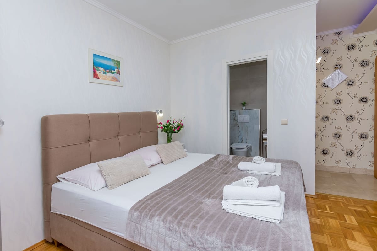 A neatly made bed with a striped blanket, a headboard, and a bedside table with a lamp and flowers.