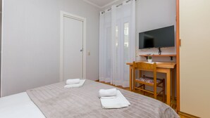 A bedroom with a bed, a desk with a chair, a television, and a door. - Apartments Tonko (Duce)