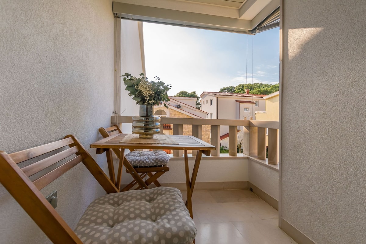 A balcony with a wooden table, a cushioned chair, and a vase with flowers.