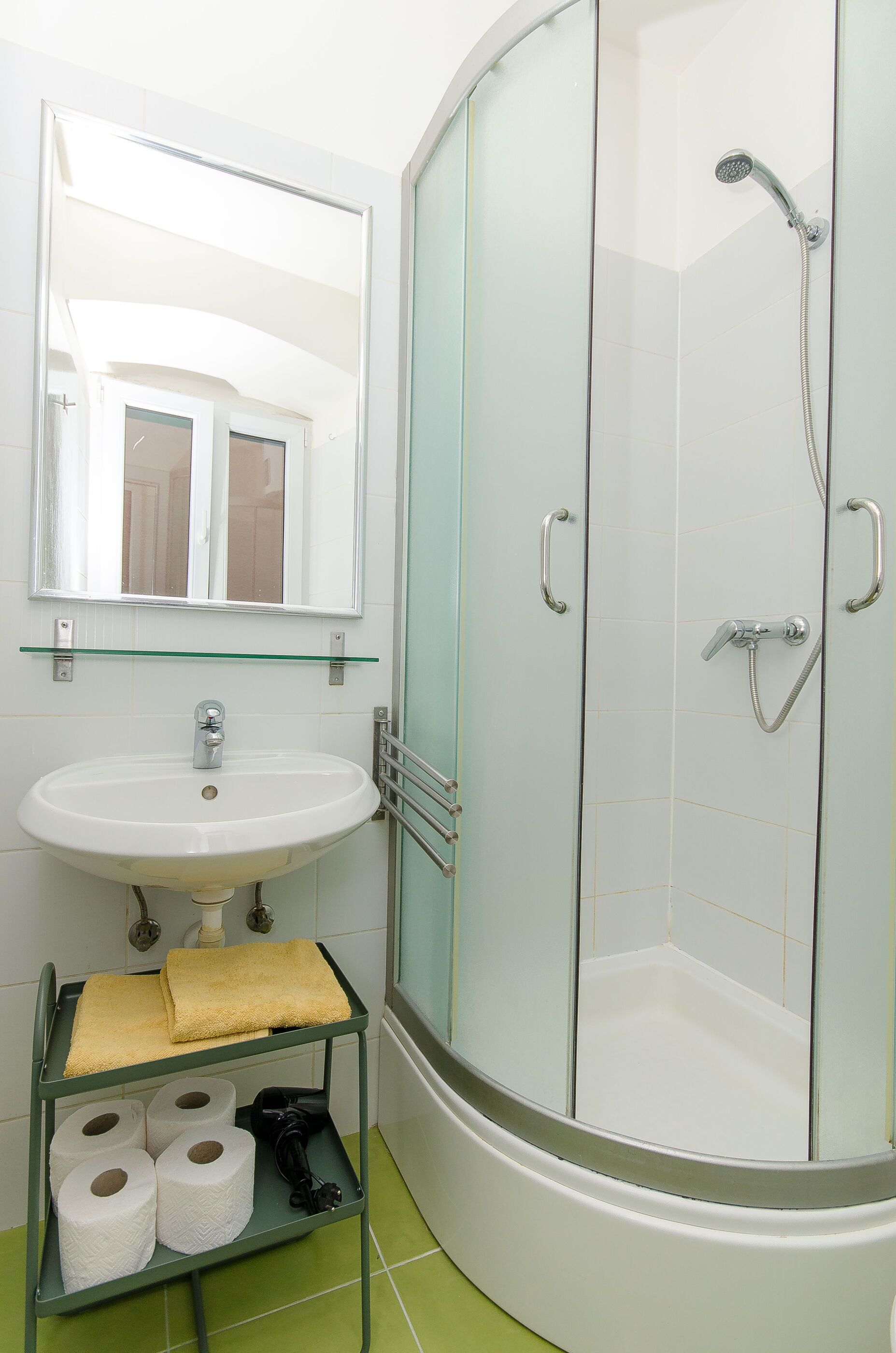 A bathroom with a glass-enclosed shower, a sink with a glass shelf above it, and a towel rack.