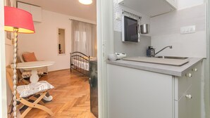 Un espacio habitable compacto con comedor que incluye una mesa y sillas, una kitchenette con lavaplatos y estufa, y una cama al fondo.