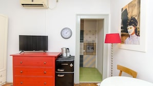 Una habitación con un aparador rojo, una minibar negra, un televisor, un reloj, una lámpara roja y un cuadro en la pared.