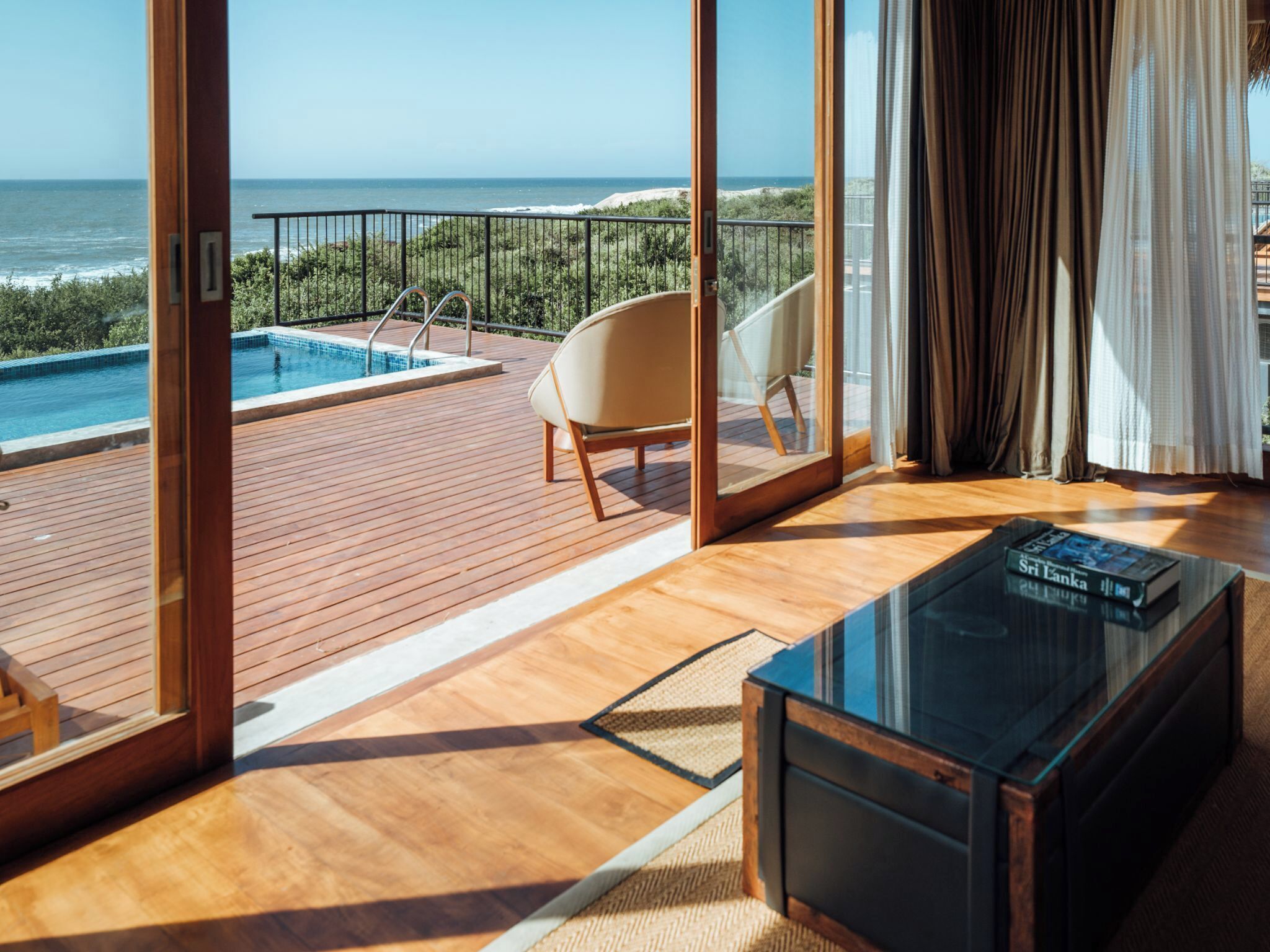 A modern room with a wooden floor, a glass coffee table, and a view of the ocean.