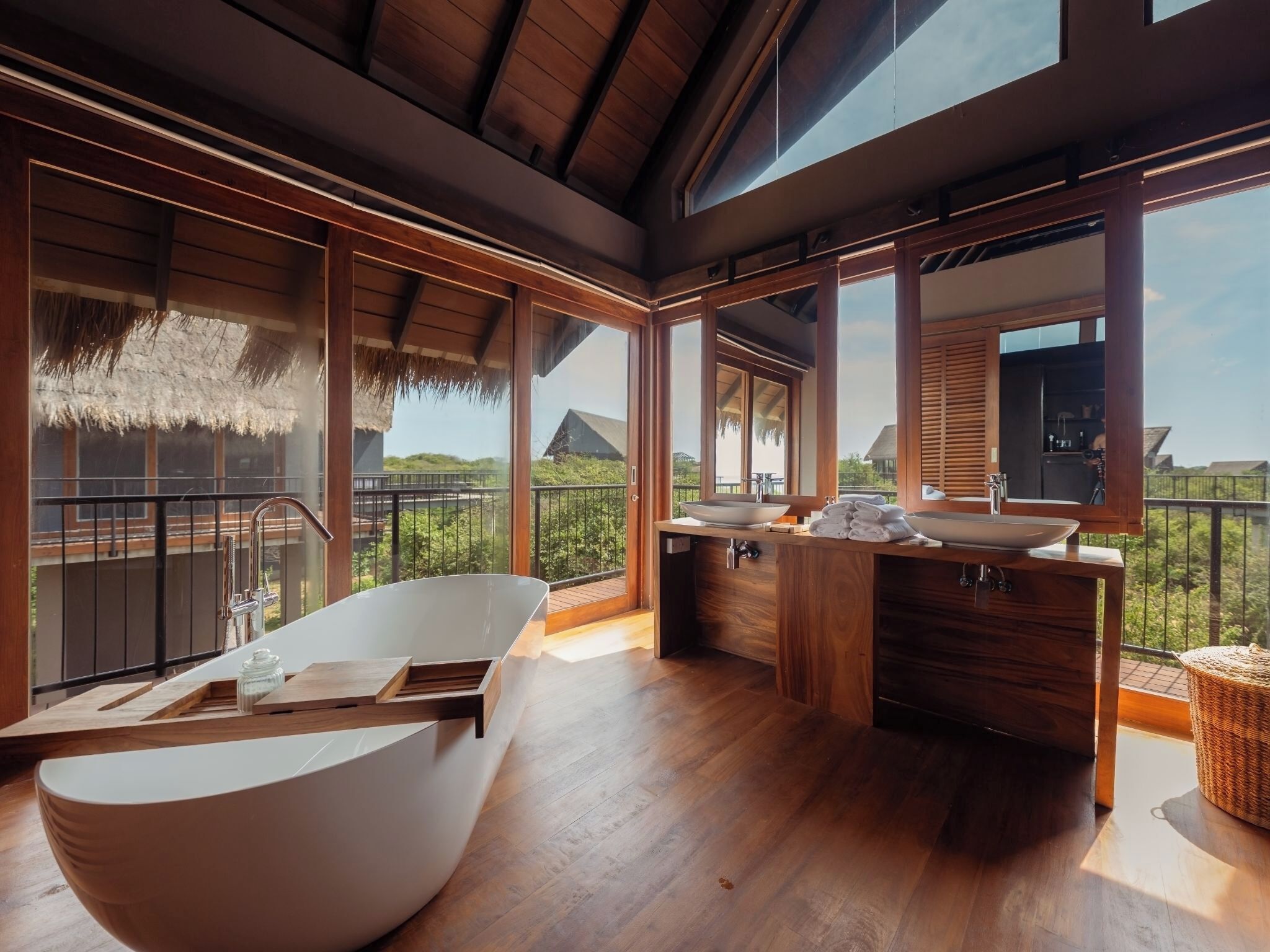 A modern bathroom with a freestanding bathtub, wooden vanity, and large windows offering a view of the surrounding landscape.