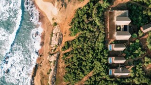 An aerial view of a coastal property with a beach, rocky terrain, and a cluster of buildings with multiple windows. - Kotiyagala Luxury Villas (Palatupana)