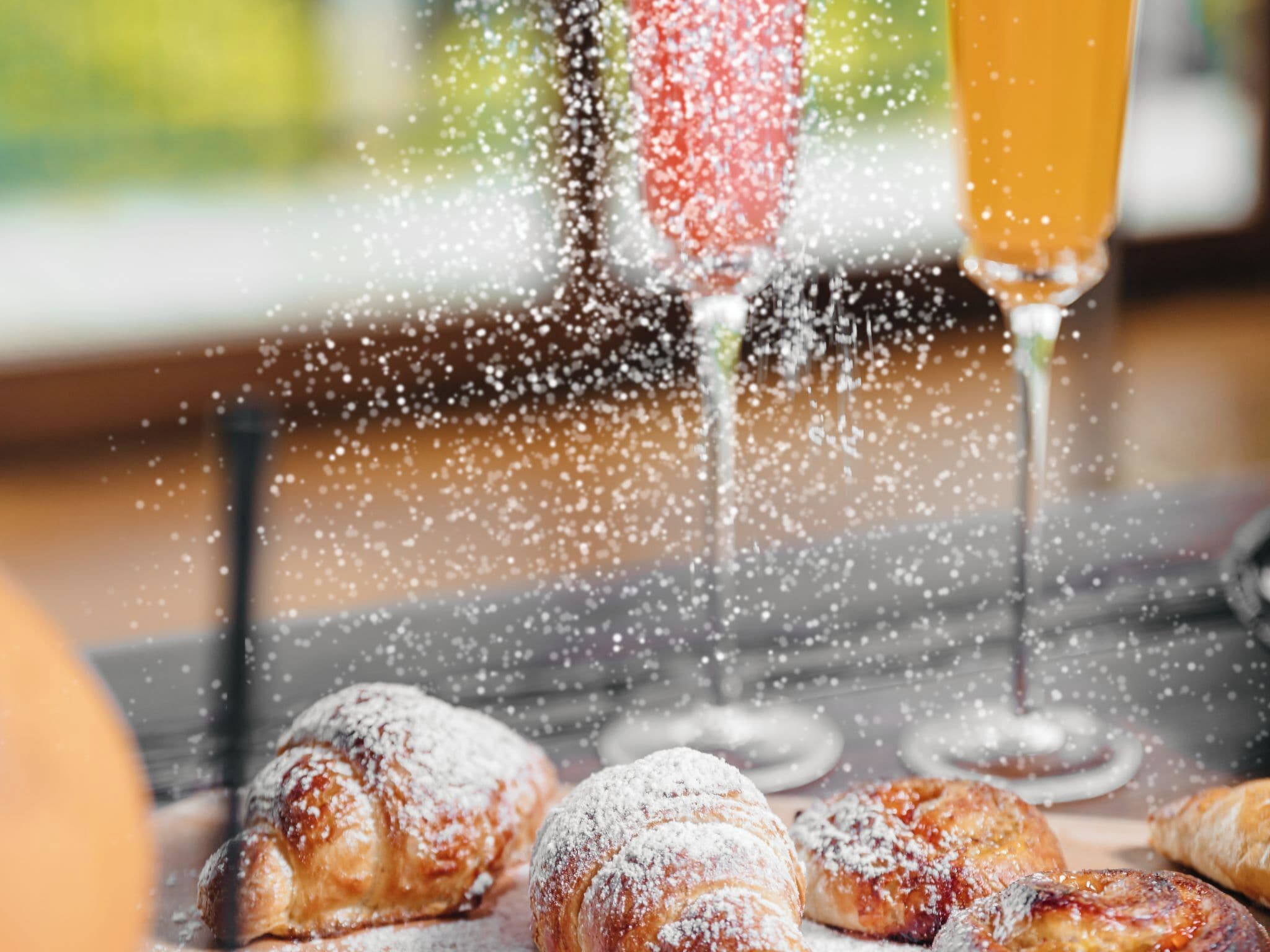 Pastries dusted with powdered sugar and a glass of orange juice on a table.