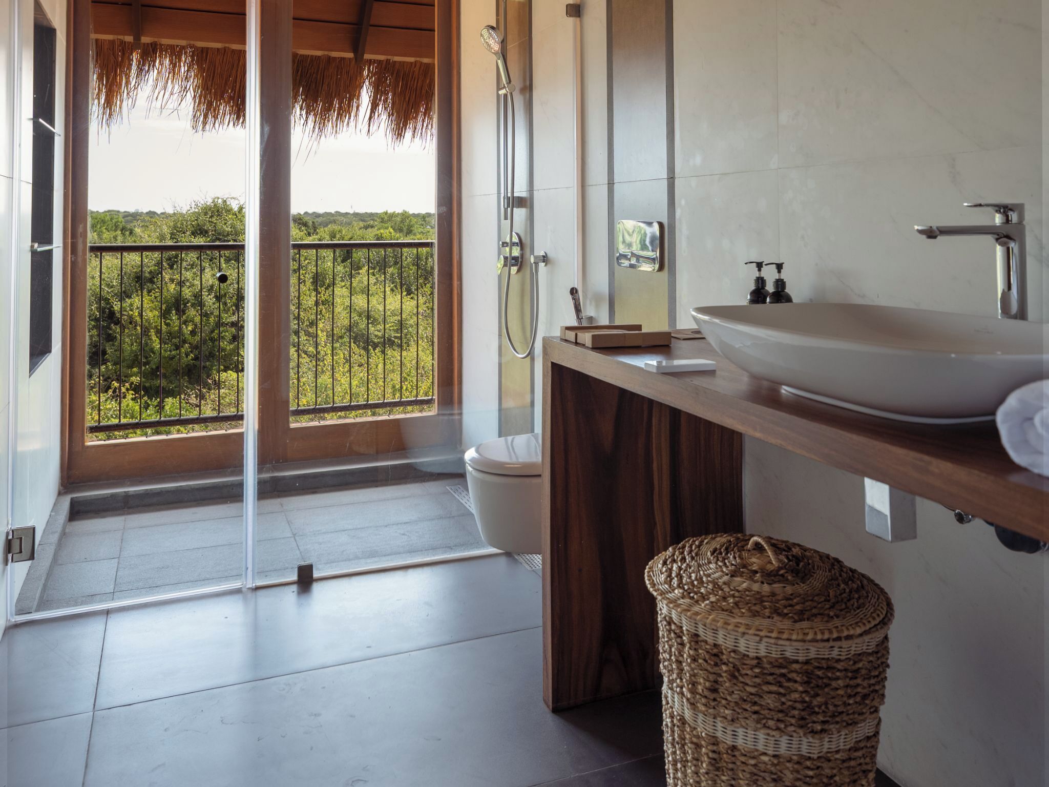 Une salle de bain moderne avec une grande fenêtre, un meuble-lavabo en bois, un lavabo blanc et un espace douche.