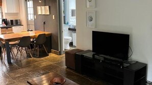 Una sala de estar moderna con una mesa de centro de madera, un televisor sobre un soporte negro, y un comedor con mesa y sillas de madera.