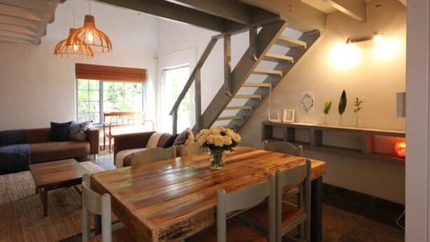 Amplia sala de estar con una mesa de comedor de madera, una escalera y un gran ventanal que proporciona luz natural.